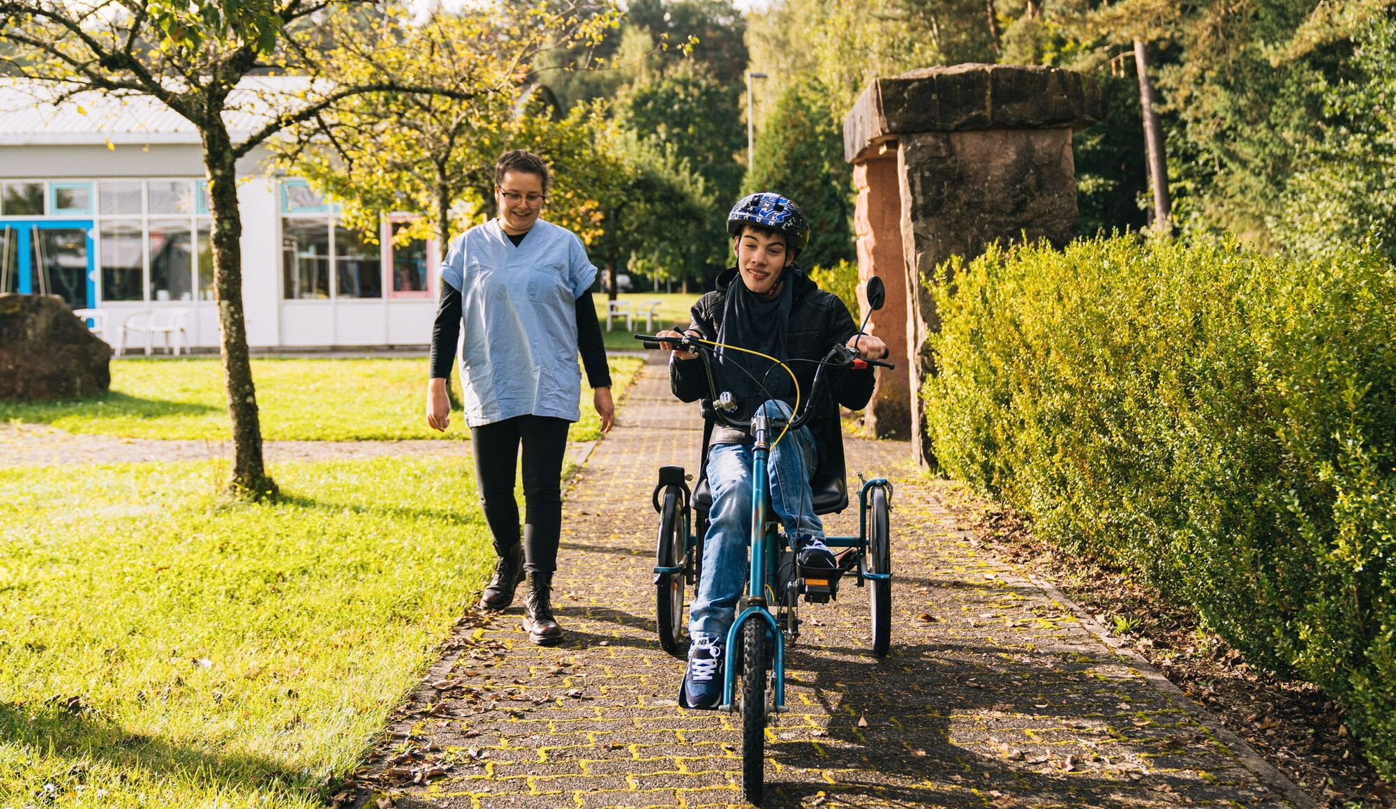 Eine Frau begleitet einen jungen Mann beim Fahrradfahren.